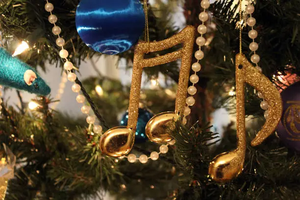 Holiday scene of close up of Christmas tree decorations. Lights, pearls, balls, and gold musical notes capture the sparkle and fun of the holiday season.