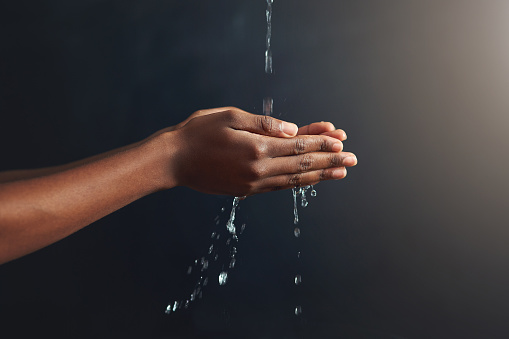 Cropped shot of hands held out under a stream of water against a grey background
