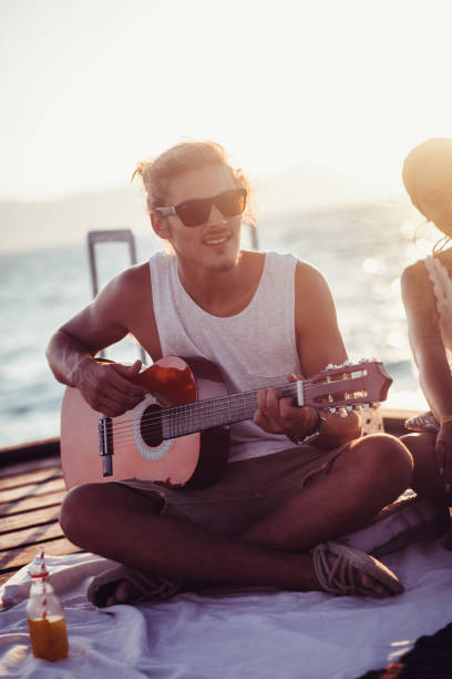 istock Young hipster man with friends playing the guitar on jetty 889513044