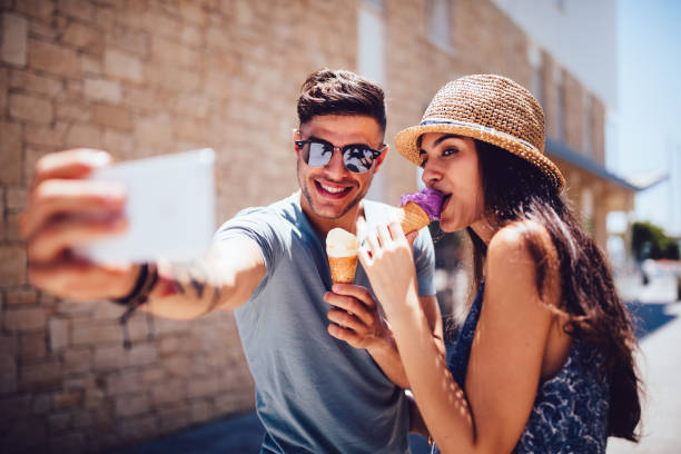 jeune couple mangeant des glaces et prendre selfies vacances d’été - été photos photos et images de collection
