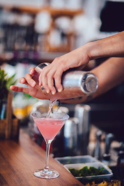 Young bartender pouring cocktail in glass at summer bar