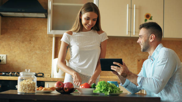 istock Attractive couple chatting in the kitchen early morning. Handsome man using tablet while his girlfriend cooking 889564164