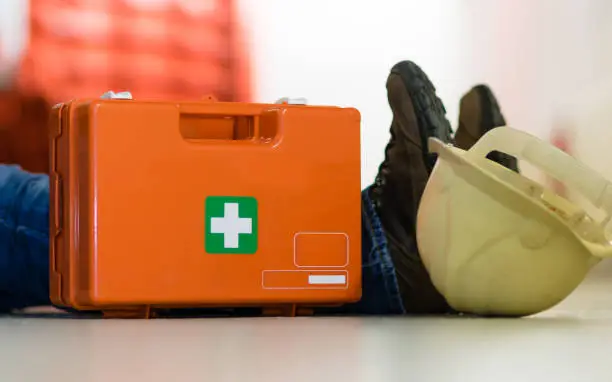 Man lying on the ground after a work accident and a first aid kit stands next to him