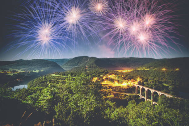 Horizontal composition photography of large colorful and beautiful blue white and red, like french flag colors, firework pyrotechnic effects in hilly nature landscape at twilight time of the day, with water river and with copy space in the sky. Taken in french Bugey mountains, in Ain, Auvergne-Rhone-Alpes region, during a celebration event like New Year or national Bastille Day 14th July.