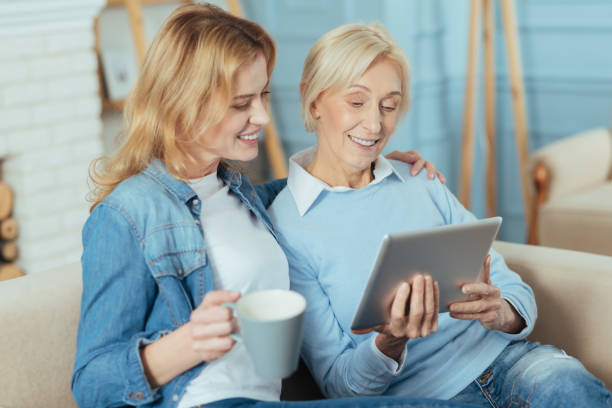 istock Happy woman holding a cup while her granny sitting with a tablet 889618880