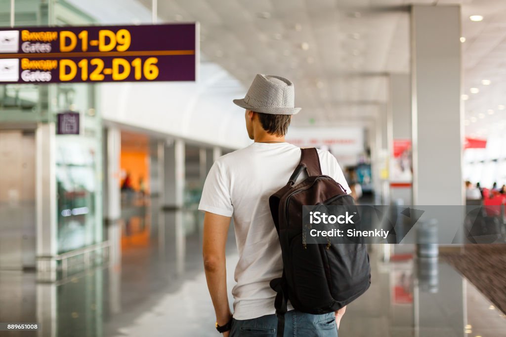 The man in the hat in the airport, business travel, passenger looking at timetable screen board Airport Stock Photo