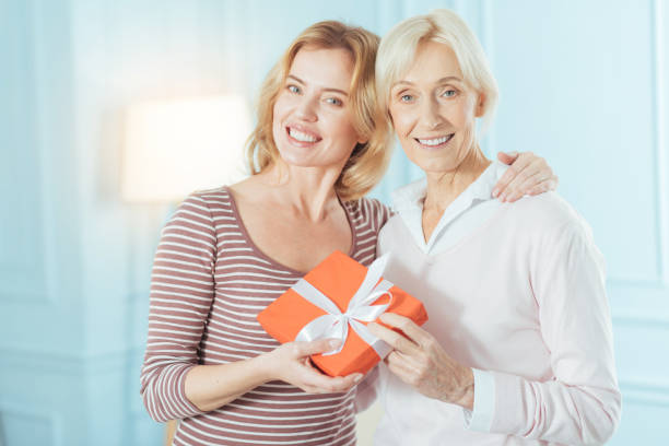 istock Cute young woman hugging her granny while holding a present 889654472
