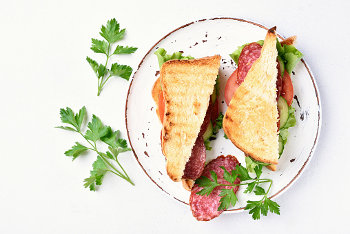 Sandwiches with salami, tomatoes, cucumber and lettuce on white background. Top view, flat lay