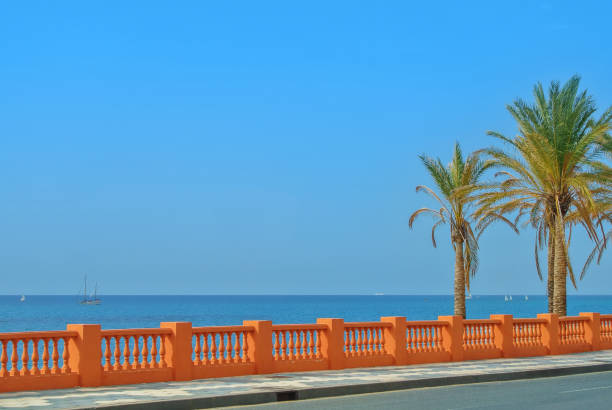 A view to Mediterranean sea from a waterfront promenade of Benalmadena beach and a road with palms at the foreground, Malaga province, Costa del Sol, Andalusia, Spain. Copy space for text. A view to Mediterranean sea from a waterfront promenade of Benalmadena beach and a road with palms at the foreground, Malaga province, Costa del Sol, Andalusia, Spain. Copy space for text. torremolinos beach stock pictures, royalty-free photos & images