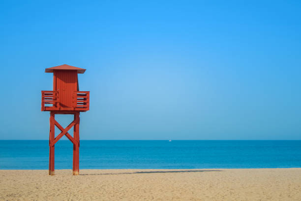 Dark red wooden lifeguard tower on the abandoned beach at Benalmadena, Malaga province, Spain. Beautiful view of the sea and sandy beach on sunny summer day with copy space. Dark red wooden lifeguard tower on the abandoned beach at Benalmadena, Malaga province, Spain. Beautiful view of the sea and sandy beach on sunny summer day with copy space. torremolinos beach stock pictures, royalty-free photos & images