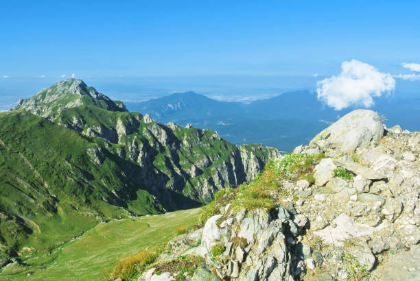 istock A panoramic view to canyon between a chain of green mountains peaks, colorful fields at the horizon and a narrow track road foot path below on sunny summer evening. Tracking in mountains. 889703280