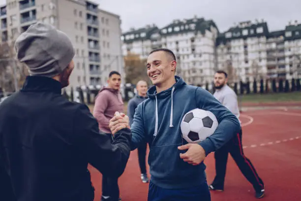 Group of men, playing soccer outdoors on the urban field, greeting before the game.