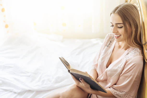 istock Young woman reading book on bed at home 889731410