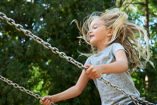 Little child blond girl having fun on a swing outdoor. Summer playground. Girl swinging high. Young child on swing outdoors
