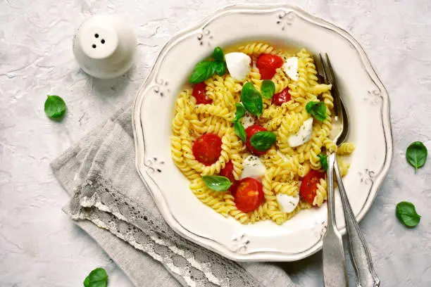 Pasta caprese with tomato,mozzarella and basil on a vintage plate over light slate,stone or concrete background.Top view.