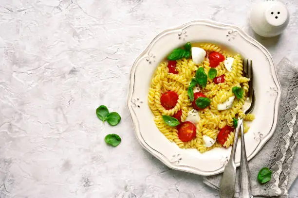 Pasta caprese with tomato,mozzarella and basil on a vintage plate over light slate,stone or concrete background.Top view.