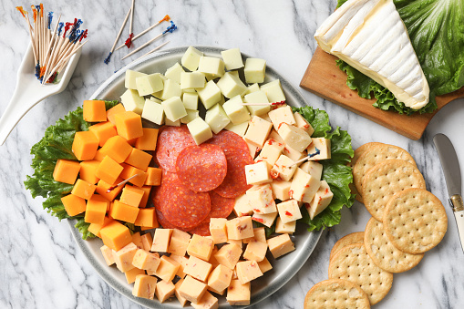 An overhead close up horizontal photograph of a sample platter of a variety of cheese bites,salami, crackers and a wedge of creamy brie cheese.