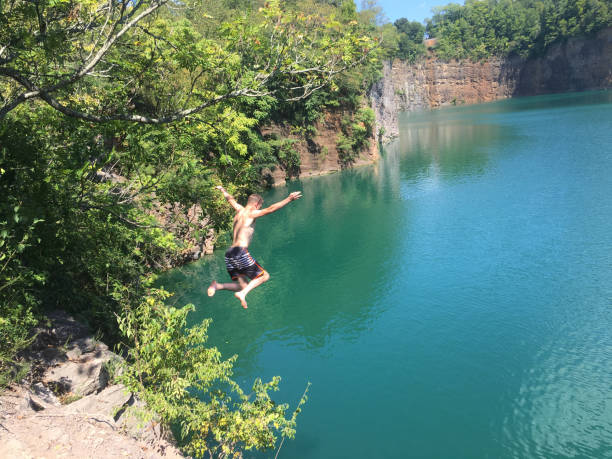 Man jumps off a cliff cooling off on a hot summer day with some recreational cliff jumping into an abandoned quarry. cliff jumping stock pictures, royalty-free photos & images