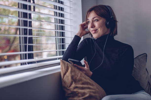 młoda kobieta słuchając muzyki w telefonie - window sill audio zdjęcia i obrazy z banku zdjęć