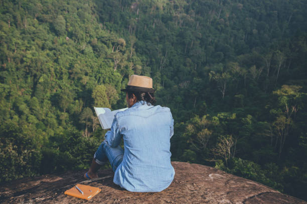 voyage de l’homme asiatique se détendre dans les vacances. sièges relax lire des livres sur les falaises rocheuses. sur la montagne. en thaïlande - writing diary nature ideas photos et images de collection