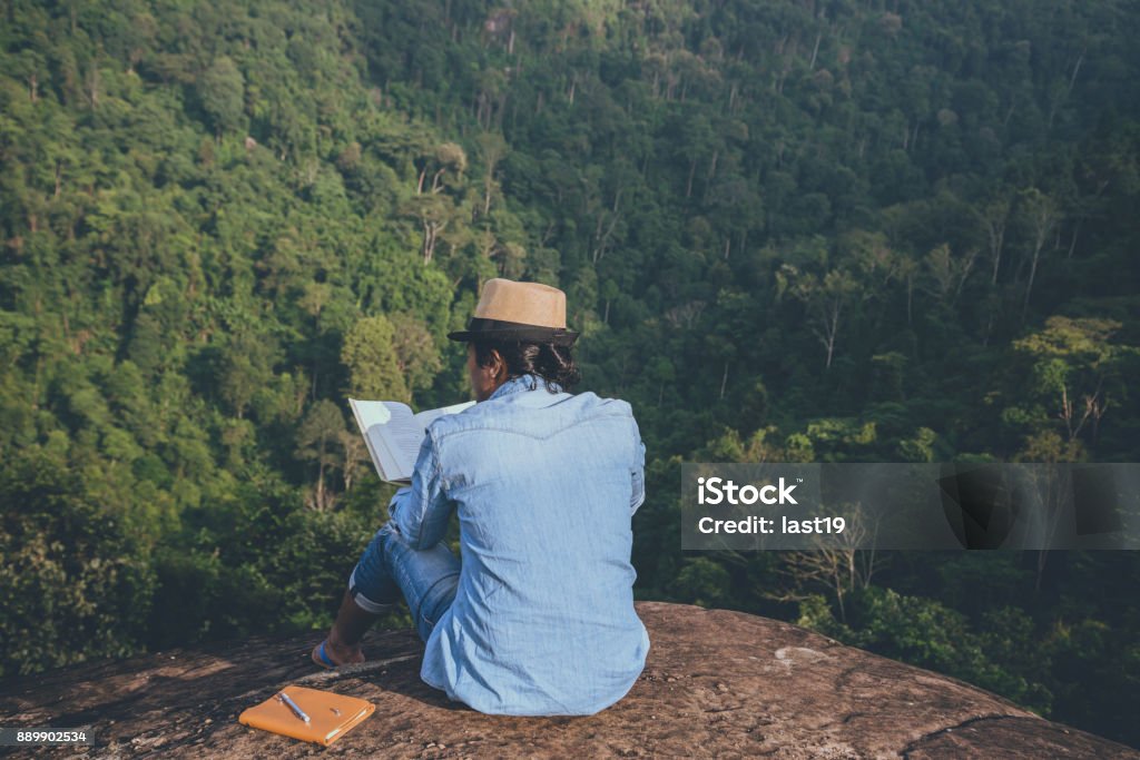 Asian man travel relax in the holiday. seats relax read books on rocky cliffs. On the Moutain. In Thailand Book Stock Photo