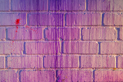 A vibrant colorful pink and purple brick wall covered in streaks and drips of glossy paint, and a red splotch of paint