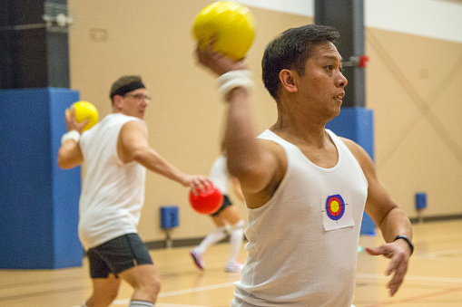 A male athlete holds a ball and a red ping-pong racket in his hand, getting ready to serve. Close-up photo of hands, without a face. Outdoors.