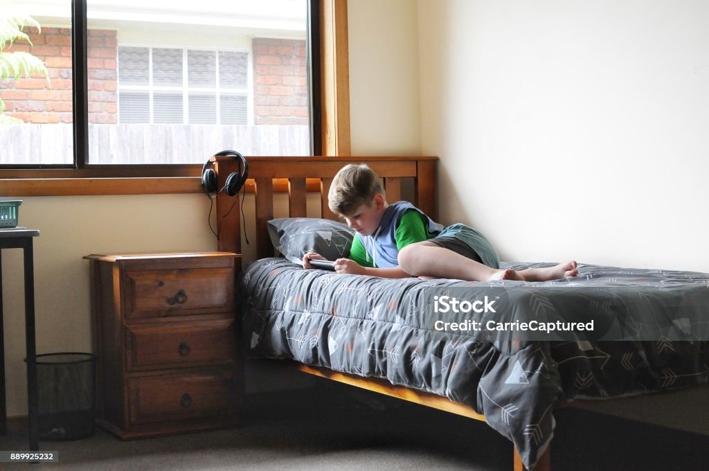 Time out Young boy using tablet device with headphones in sunny bedroom. Bedroom Stock Photo