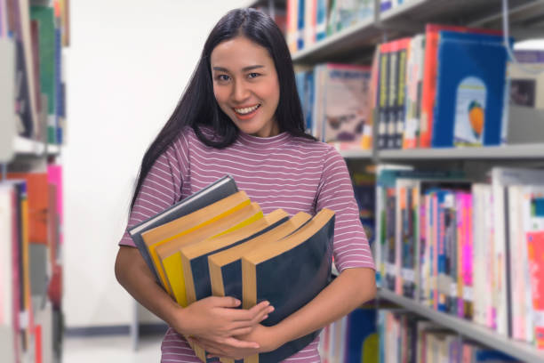 istock Asian beautiful young woman student holding stack of old books in library. 889938404