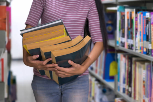 istock Asian student holding stack of books in library. 889938408