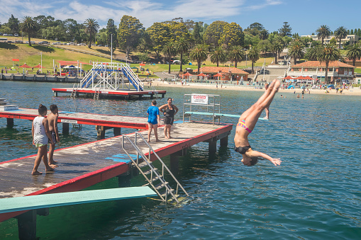 Geelong, Australia - February 4, 2017: A girl does a backflip from a diving board at the Eastern Beach Swimming Enclosure.