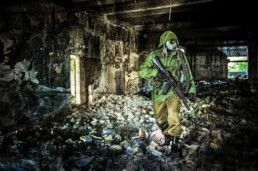 Unrecognizable soldier with a gas mask and a rifle in a warehouse (chemical and biological weapons concept)