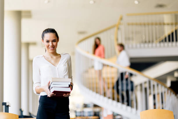 istock Beautiful woman holding books in a library 889976596
