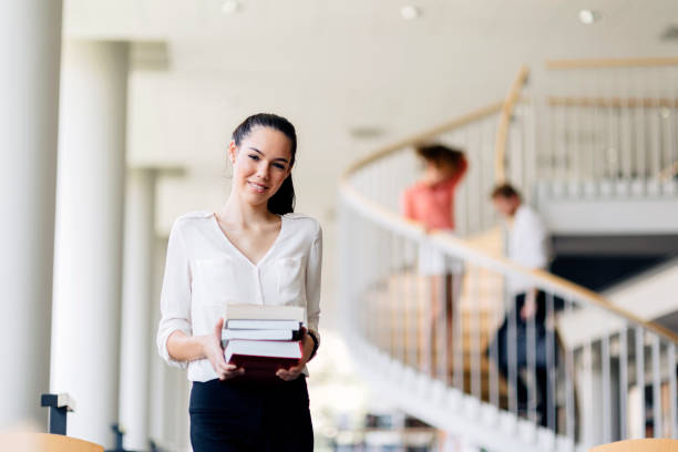 istock Beautiful woman holding books in a library 889976632