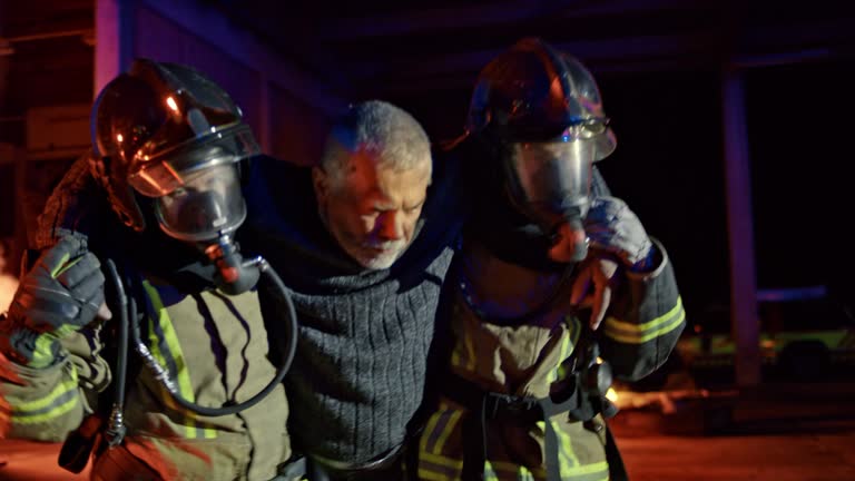 Two firefighters carrying a man out of the burning building at night