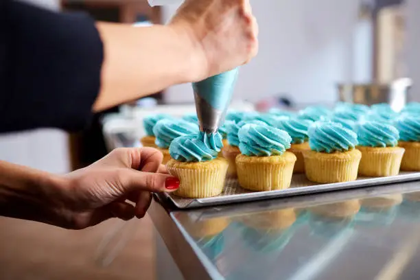 The confectioner's hands are decorated with a cream of pipping bug capkake on the kitchen table.