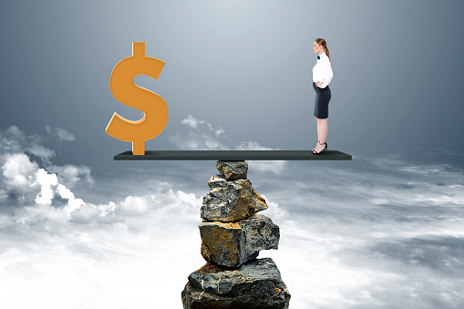 Businesswoman and dollar sign on seesaw above stack of rocks