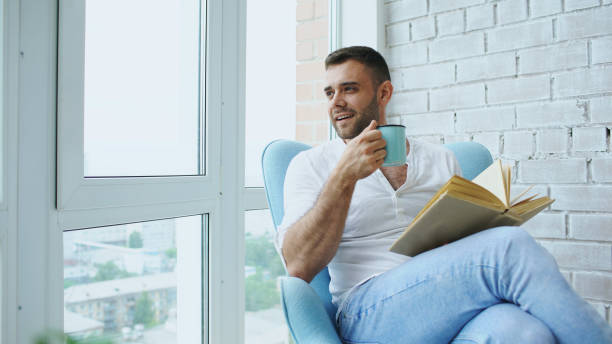istock Young man read book sitting on balcony in modern apartment 890104760