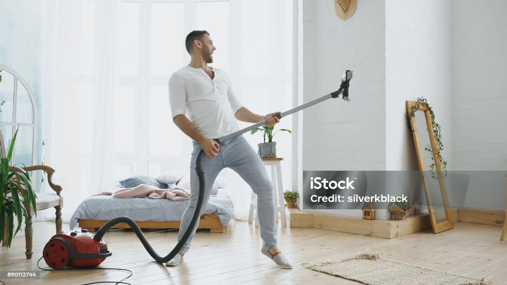 Young man having fun cleaning house with vacuum cleaner dancing like guitarist Dancing young man having fun cleaning house with vacuum cleaner at home Vacuum Cleaner Stock Photo