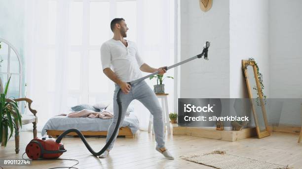 Young Man Having Fun Cleaning House With Vacuum Cleaner Dancing Like Guitarist Stock Photo - Download Image Now