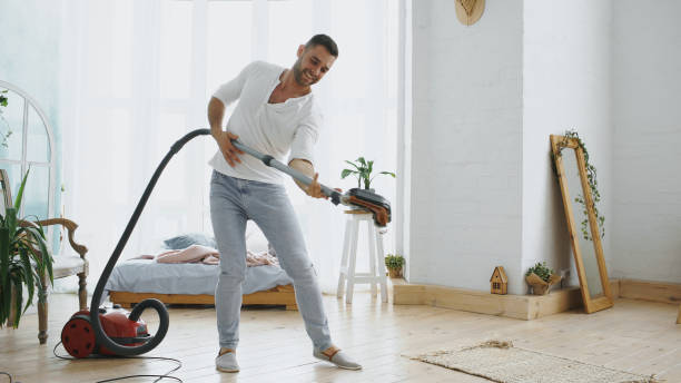 istock Young man having fun cleaning house with vacuum cleaner dancing 890114836