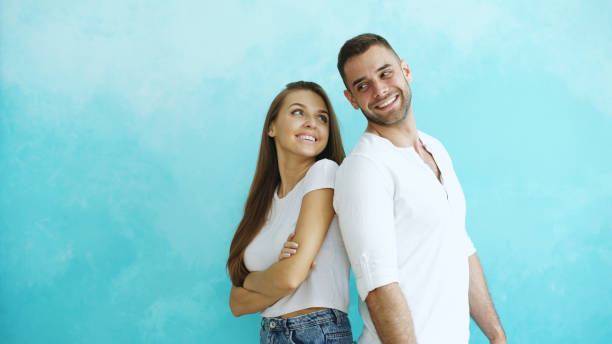 istock Young couple standing back to back flirting each other on blue background 890118288