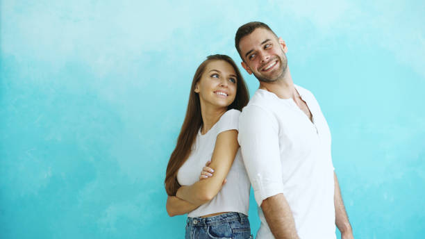 istock Young couple standing back to back flirting each other on blue background 890118310