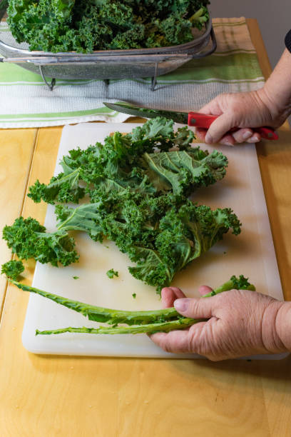 istock Hand holding two green kale ribs cut from leaves on a white cutting board 890121176