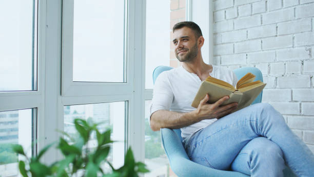 istock Young man read book sitting on balcony in modern apartment 890126958