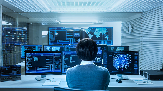 In the System Control Data Center Technician Operates Multiple Screens with Neural Network and Data Mining Activities. Room is Light and Full of Monitors with Working Neural Network on Them.