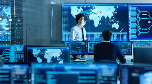 istock In the System Control Room Manager Holds a Briefing for His Staff Member. They're Work in Data Center and are Surrounded by Multiple Screens Showing Maps, Logistics Data. 890155098