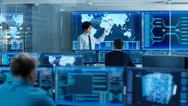 istock In the System Control Room Manager Holds a Briefing for His Staff Members. They're Work in Data Center and are Surrounded by Multiple Screens Showing Maps, Logistics Data. 890155100
