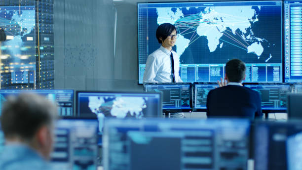 istock In the System Control Room Manager Holds a Briefing for His Staff Members. They're Work in Data Center and are Surrounded by Multiple Screens Showing Maps, Logistics Data. 890155110