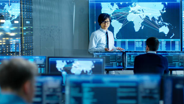 istock In the System Control Room Manager Holds a Briefing for His Staff Members. They're Work in Data Center and are Surrounded by Multiple Screens Showing Maps, Logistics Data. 890155120